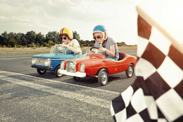 Two boys in pedal cars crossing finishing line on race track